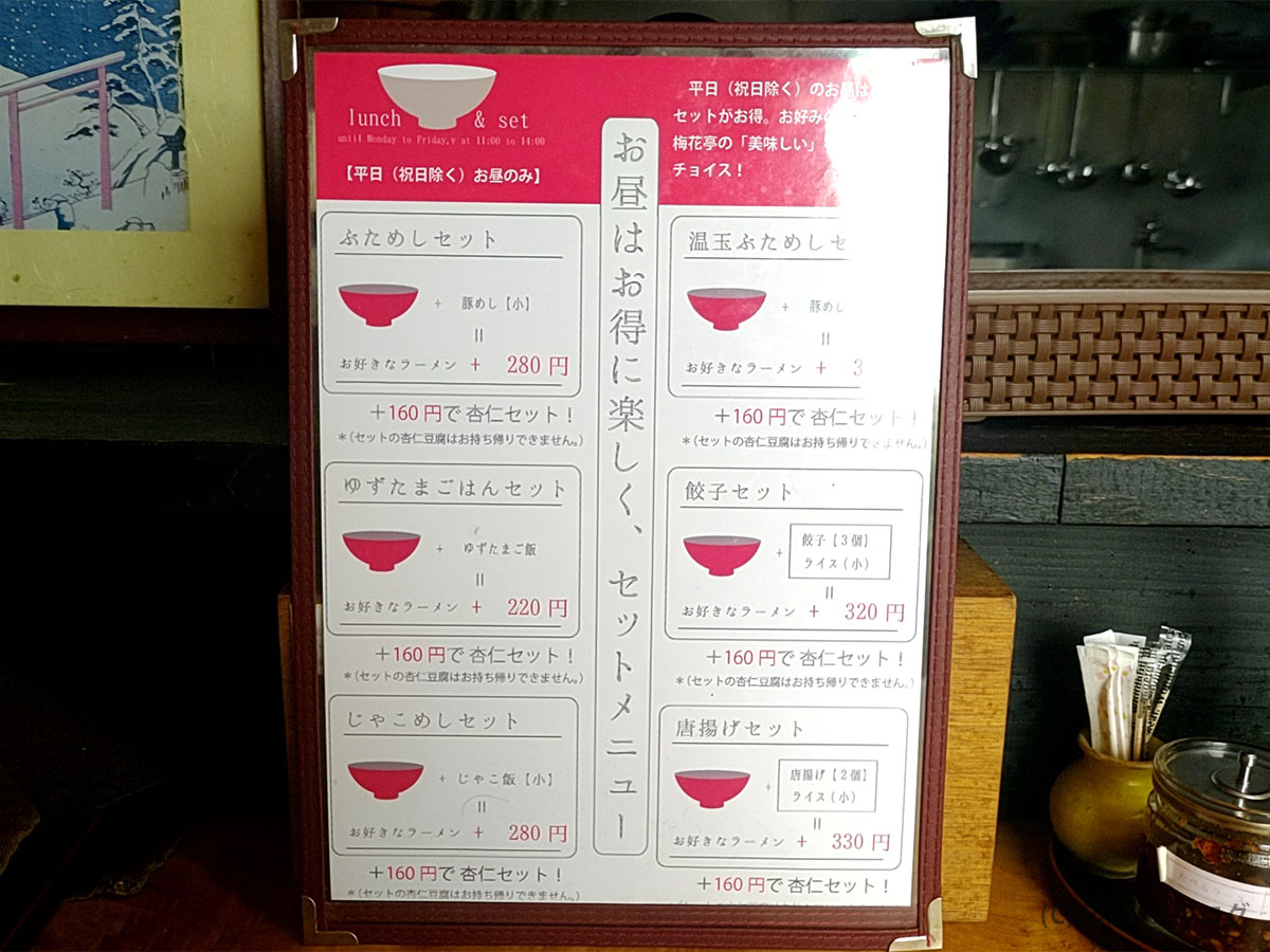 「お昼はお得に楽しくセット!」と題した梅花亭のランチメニュー。豚めしや餃子セットなどが手書き風に並ぶ。