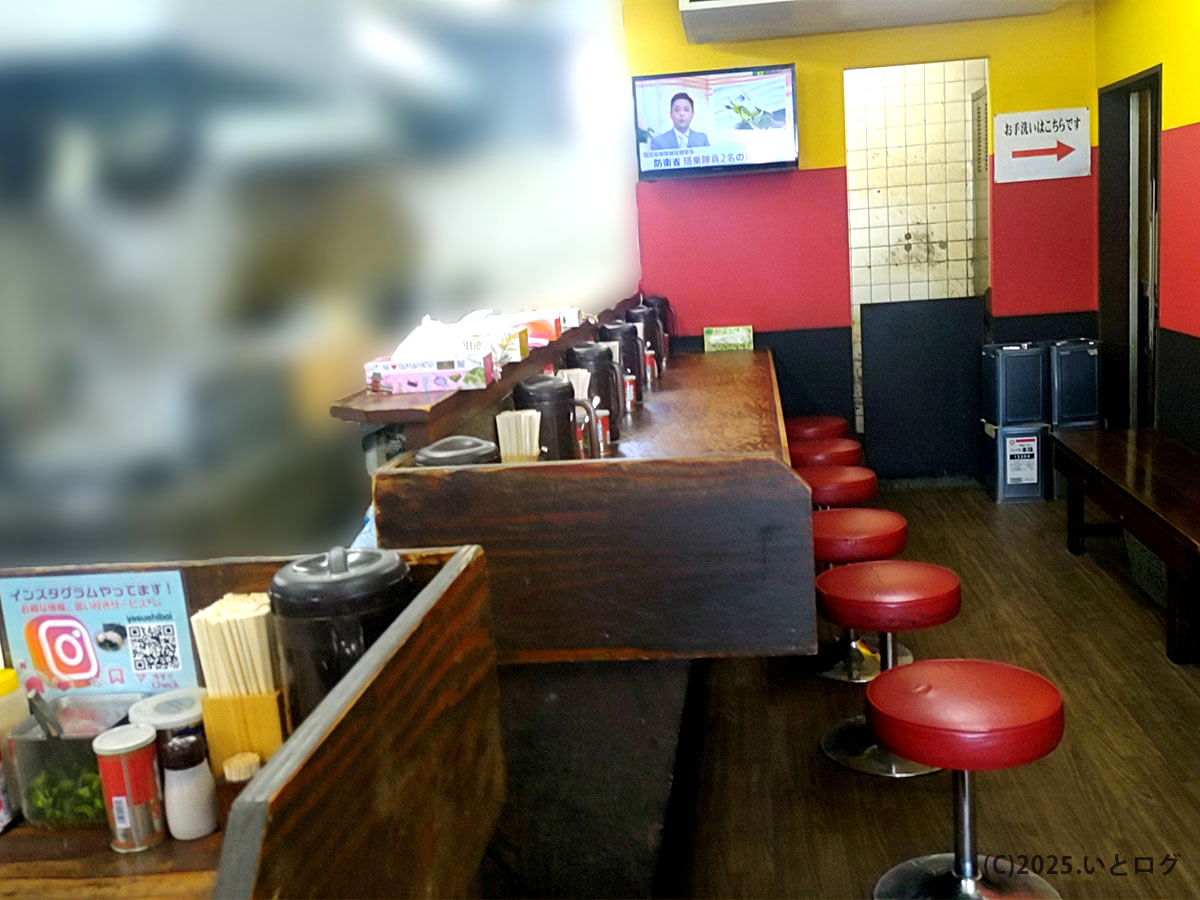 赤と黄色の壁が印象的な「ヤスシボーイ 周南市」の店内。カウンター席が並び、テレビが流れる昭和レトロな雰囲気のラーメン店。下松エリアで人気の家系ラーメンを味わえる。