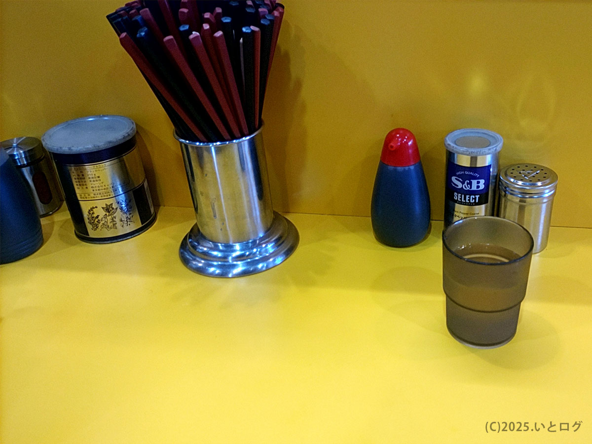 ラーメン二郎 八王子野猿街道店2の卓上調味料と箸。黄色いカウンターが印象的な店内風景