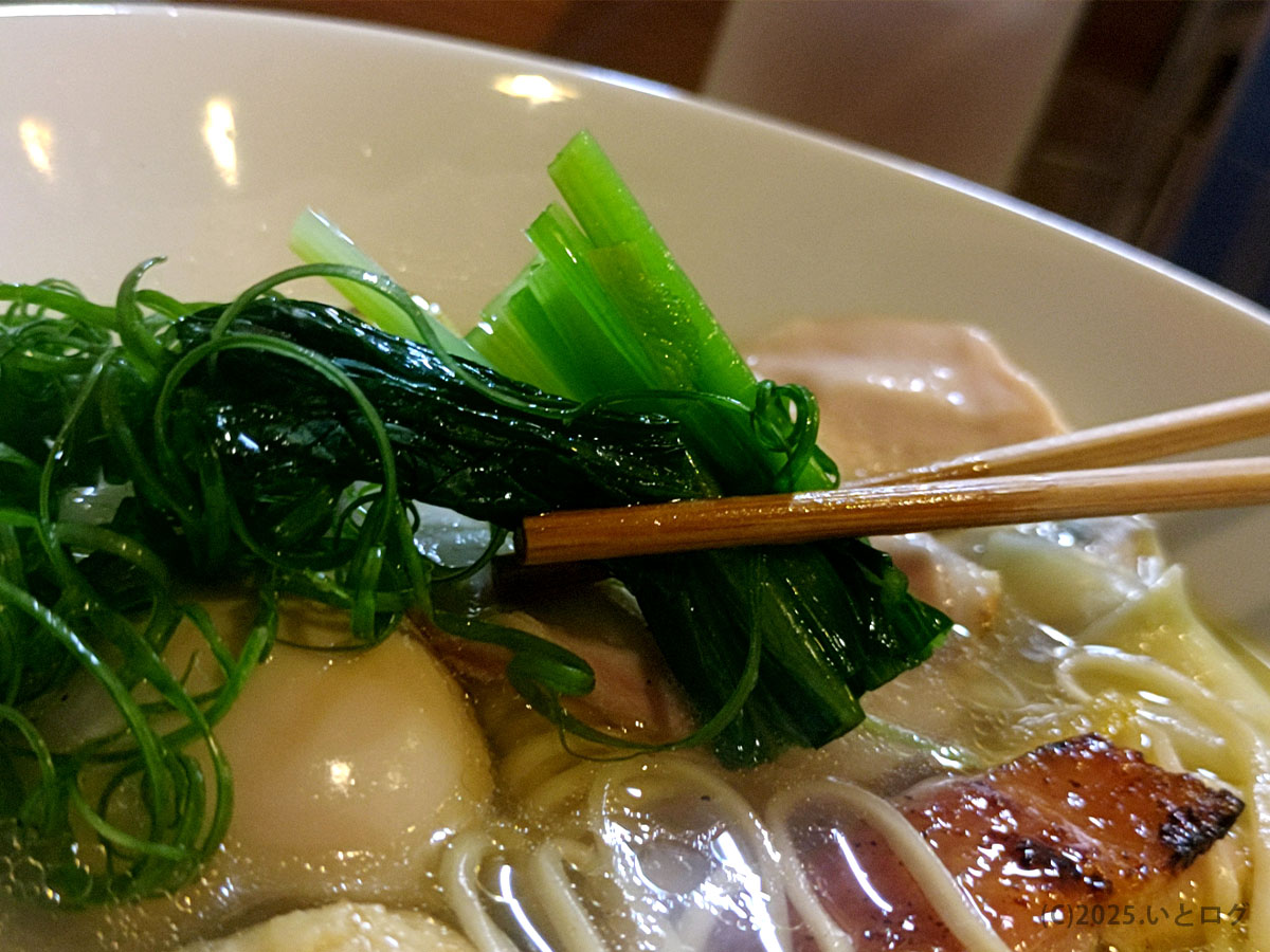 山梨県甲府市にある人気店「鶏そばAkari」の鶏白湯ラーメン。青菜とネギを箸で掬い上げた場面で、澄んだスープの透明感と丁寧な盛り付けが伝わる。山梨の鶏白湯を探している人や「甲府 ラーメン 人気」を調べている人に向けた一枚。