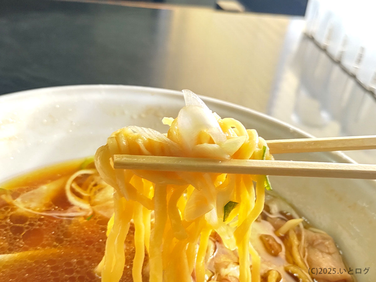自家製ちぢれ麺をリフトアップする瞬間。黄金色の醤油スープとネギが映える、手打 焔の人気メニュー紹介写真
