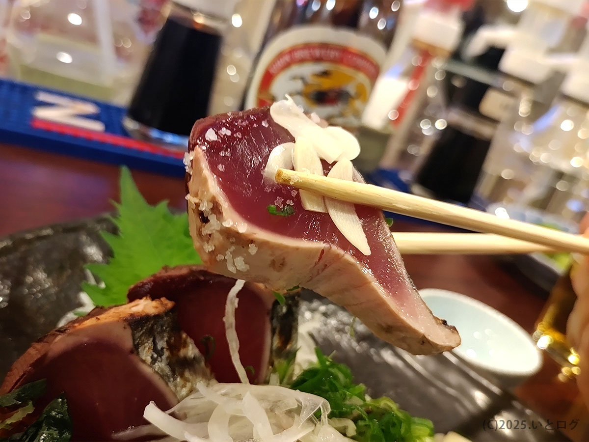 箸で持ち上げた藁焼きカツオタタキの断面。表面香ばしく中心はレア、薬味が香る室戸屋ジロー看板料理のアップ写真(レビュー向け)。