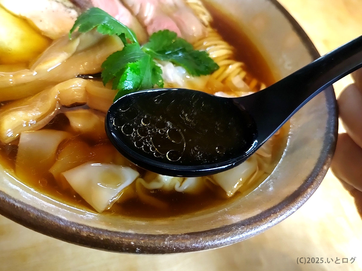 琥珀色の澄んだスープを黒レンゲですくったところ。地鶏だしの香りが立つ梅花亭の一杯。