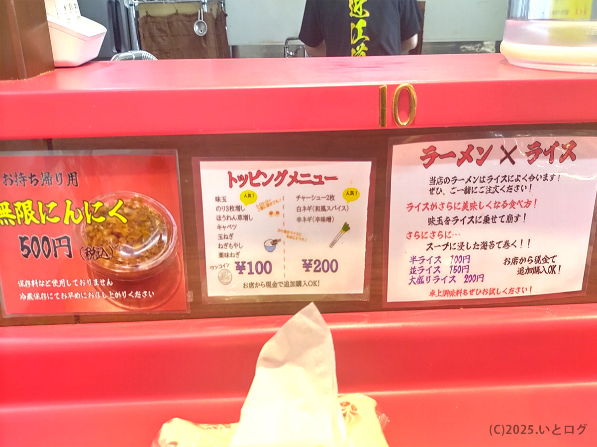 カウンターに「ラーメン×ライス」の案内とトッピング表、奥にスタッフの背中。近江道家×食いしん坊の組み合わせをそそる一枚。