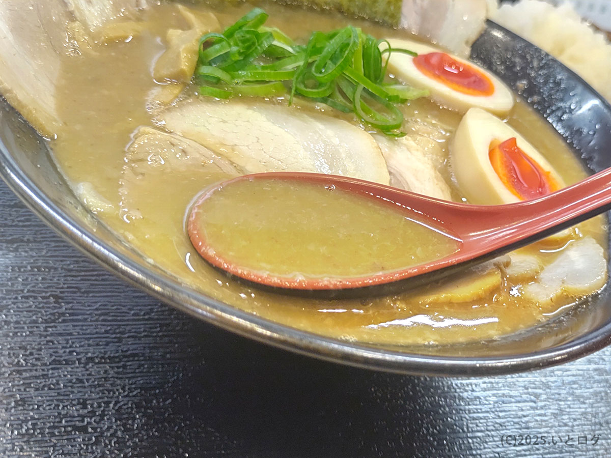 レンゲですくったスープはとんこつ魚介の旨味が凝縮した濃厚な味わい。大判チャーシューや味玉、青ねぎが浮かび、ラーメン与七 豚そばの迫力ある一杯を表している。