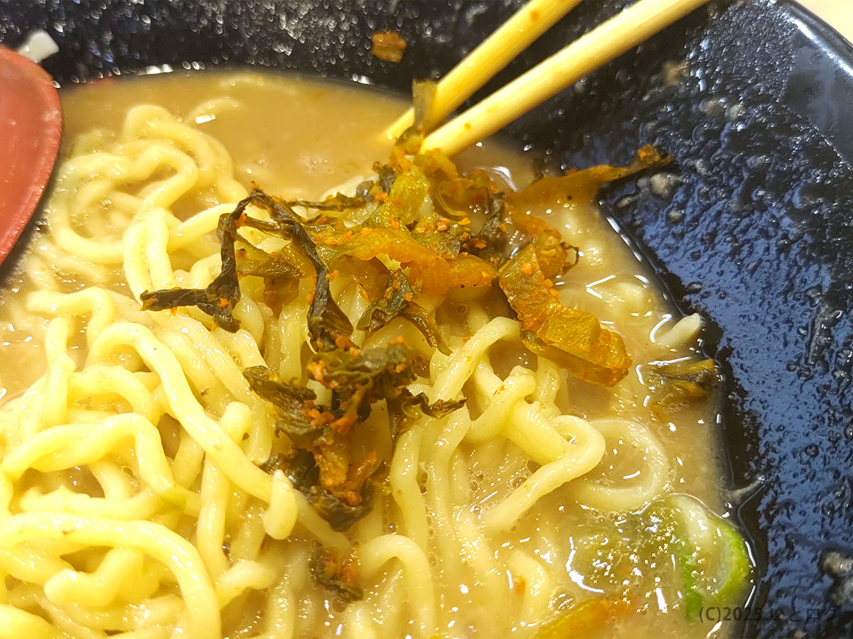 豚そばを食べ進めた後のスープに、卓上の辛子高菜を入れてアクセントを加えた様子。ラーメン与七 堅田店では味の変化を楽しめる薬味が豊富で、草津店でも同様に利用できる。