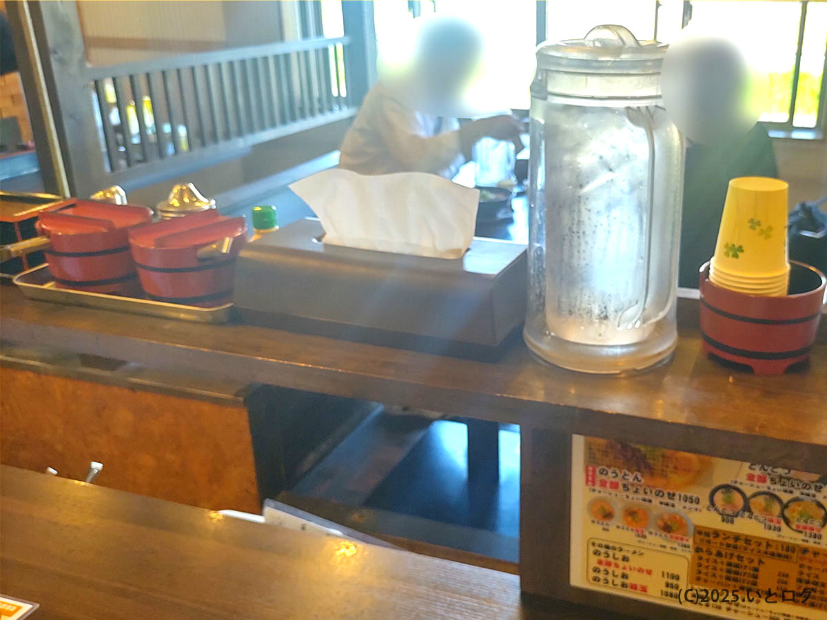 卓上の紅しょうが・白ごま・辛子高菜など調味料と給水ポット。博多ラーメンらしいセット感がある真咲雄のカウンター