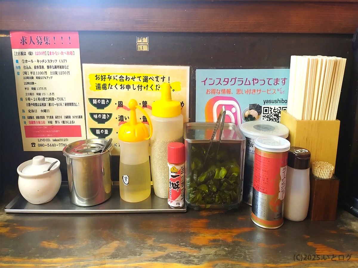「ヤスシボーイ」のカウンター卓上調味料。刻み青唐辛子やおろしニンニクなど、家系ラーメンらしい味変アイテムがずらり。下松の常連客にも愛される自由度の高いカスタマイズ。