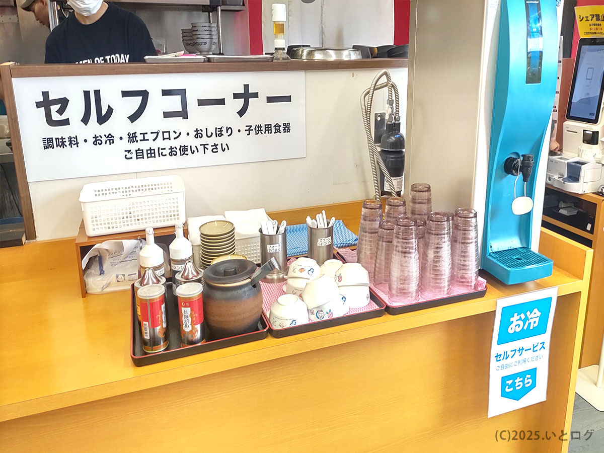 ラーメンオブトゥデイ下松店のセルフコーナー。調味料や紙エプロン、お冷のセルフサービスが並ぶ。ファミリーでも利用しやすい明るい店内。階杉ラーメン系列らしい心配り。