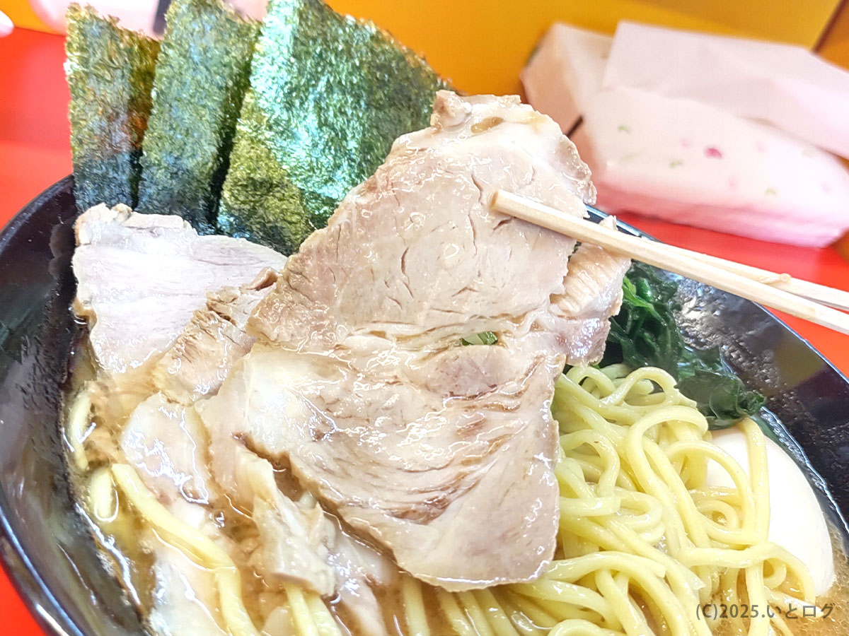 成瀬家のチャーシューを箸で持ち上げた場面。大判で柔らかく煮込まれた肉がスープと絡み、岡山家系ラーメンのボリューム感を物語る。