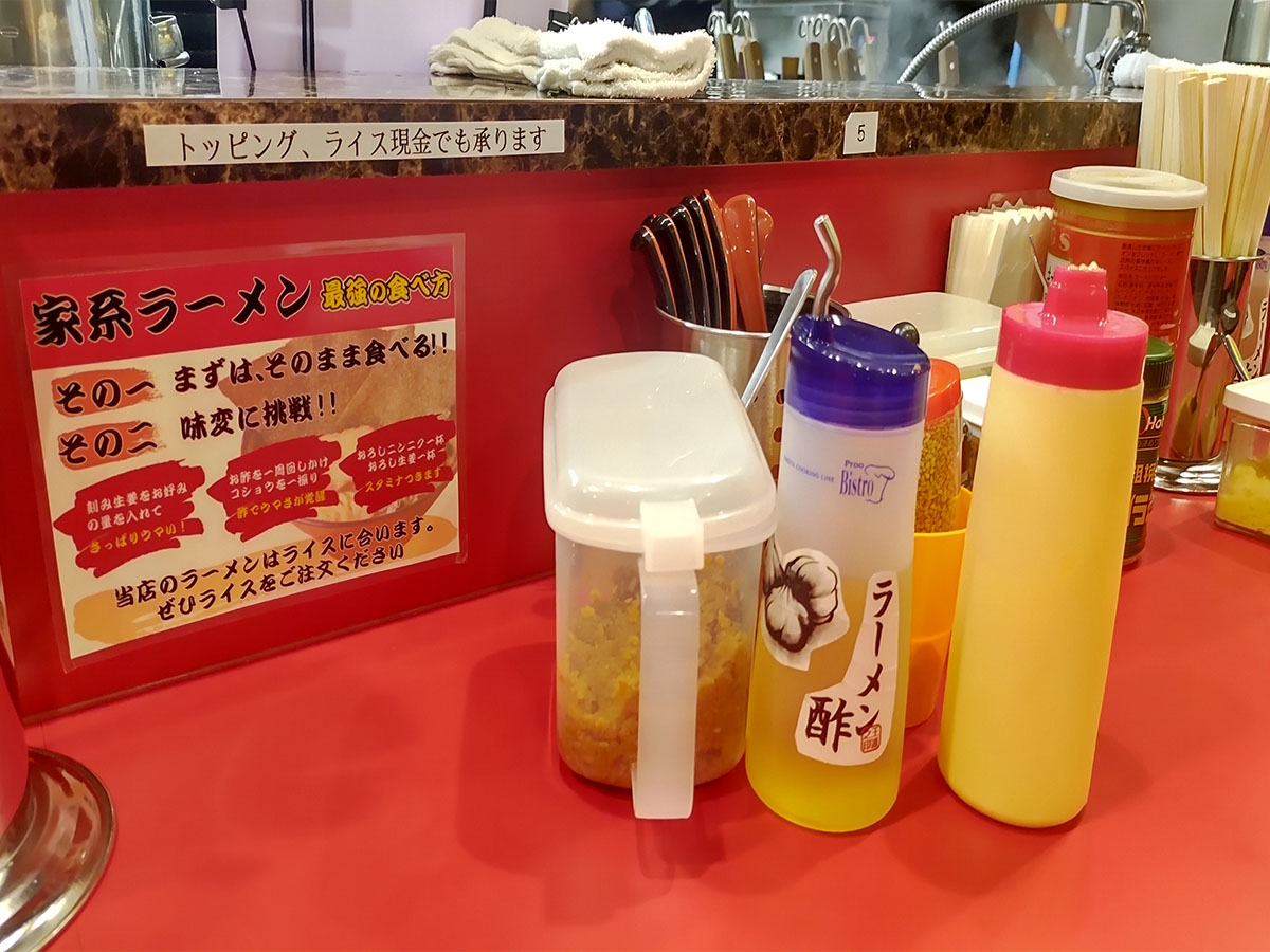 鬼道家のカウンターに並ぶ調味料セットと「家系ラーメン最強の食べ方」案内。ラーメン酢やニンニクで味変を楽しむのが鬼道家流。