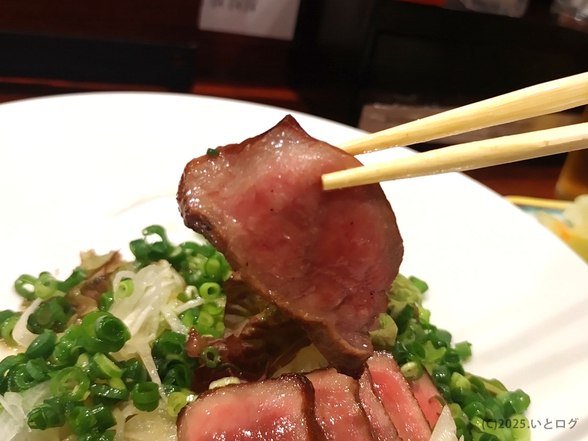 牛たん料理 閣 ブランドーム本店の牛たんたたきを箸で持ち上げた様子。中心がレアでしっとりした断面が見え、ねぎをたっぷり添えた人気メニュー。仙台で牛タンを味わうなら外せない一品。