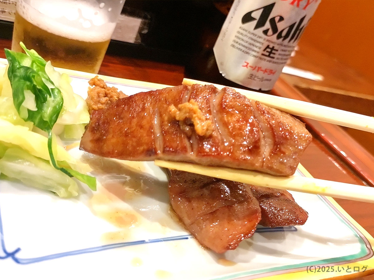 厚切り焼き牛タンを箸でつまんだアップ。表面は香ばしく焼かれ、噛み応えのある食感が伝わる。付け合わせの漬物と合わせて楽しむ仙台名物で、ブランドーム閣ランチや予約客にも定番。
