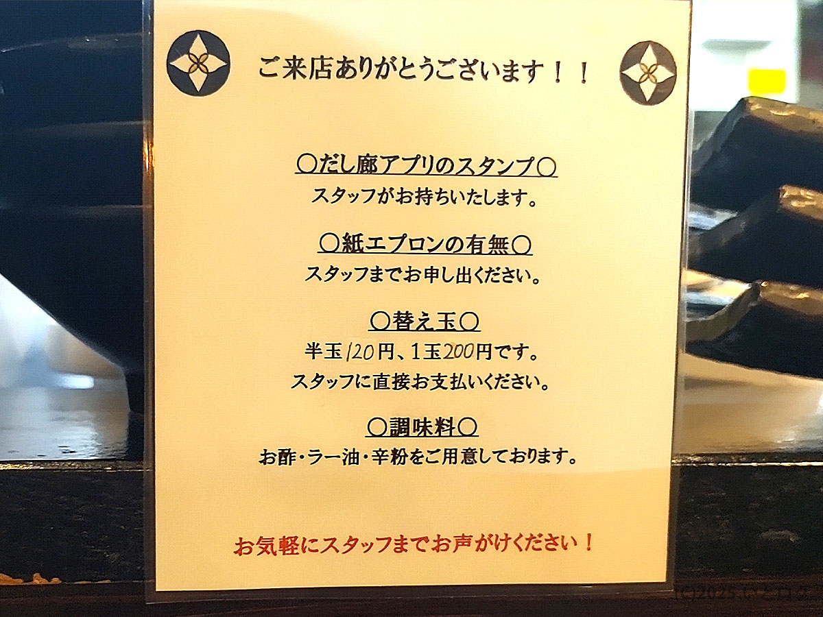 だし廊 本店の案内札。紙エプロンや替え玉の案内、調味料の利用方法など、丁寧な接客が感じられる内容。