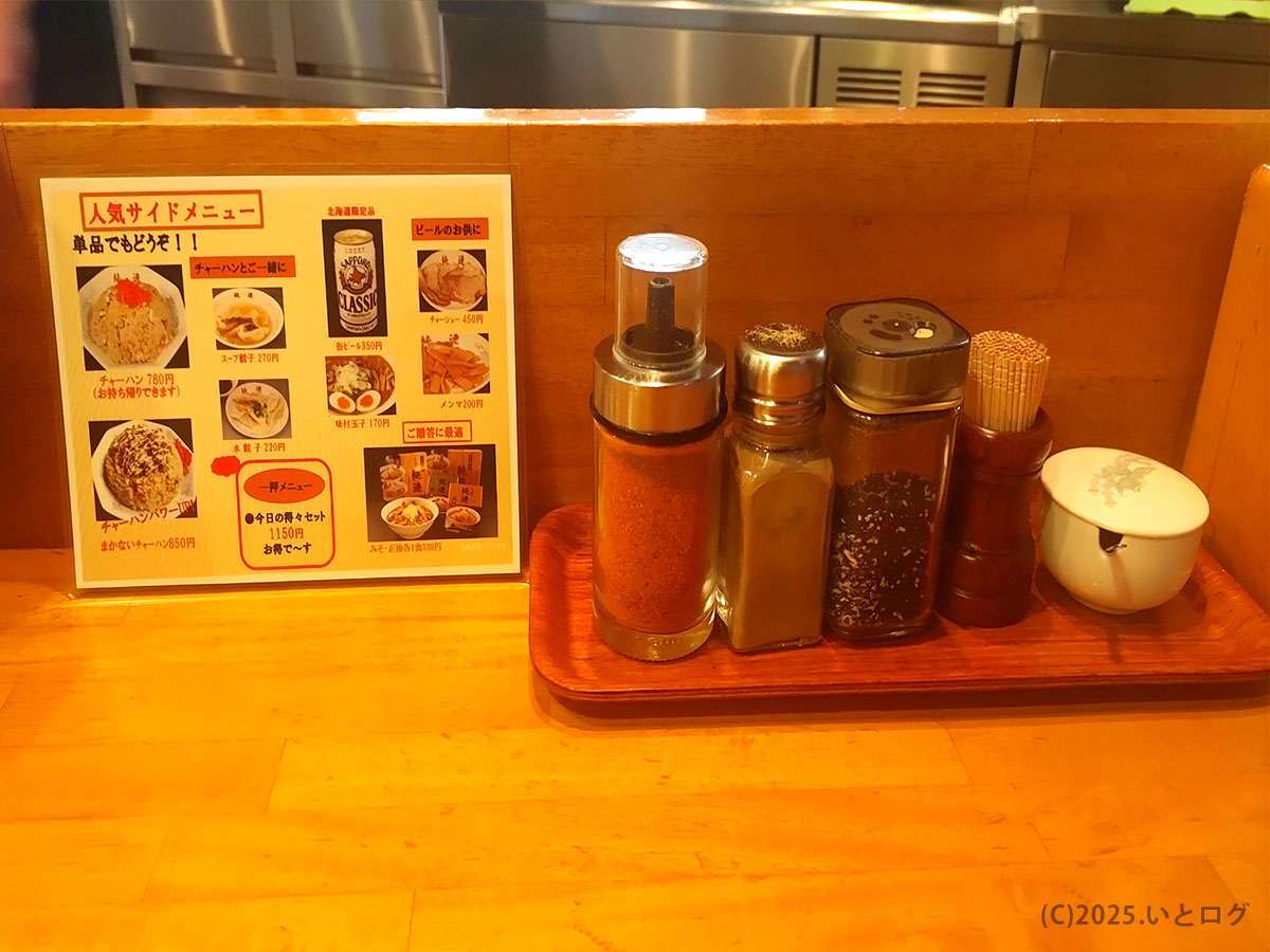 さっぽろ純連 仙台店のカウンターに並ぶ七味や胡椒などの調味料と、チャーハンやスープ餃子などの人気サイドメニュー一覧。仙台でラーメンと一緒に楽しめる定番構成。