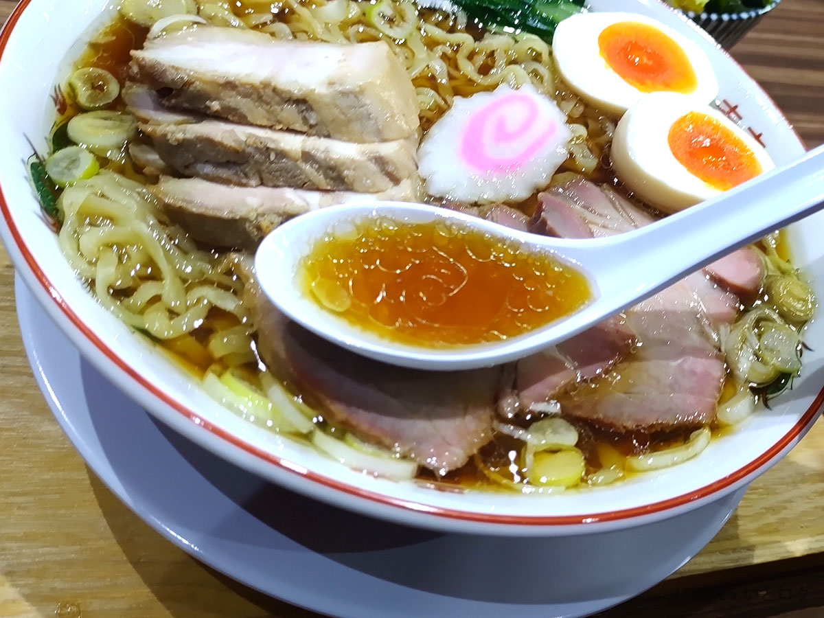 レンゲですくった琥珀色の醤油清湯。ラーメン じん ない 山梨のコクと香りが艶で伝わるスープクローズアップ。
