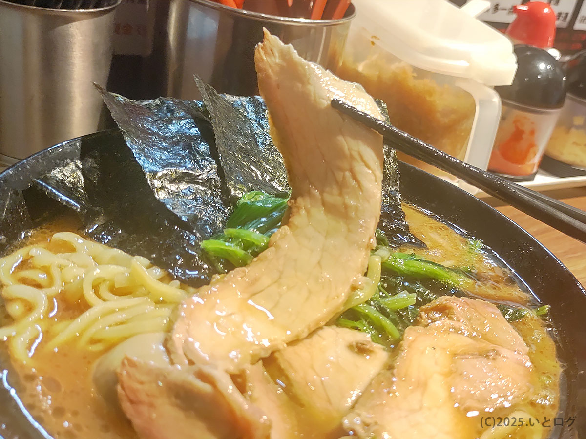 輝道家 水道橋店のチャーシューを箸で持ち上げたアップ。脂身の旨味が家系スープに溶け込む仕上がり。