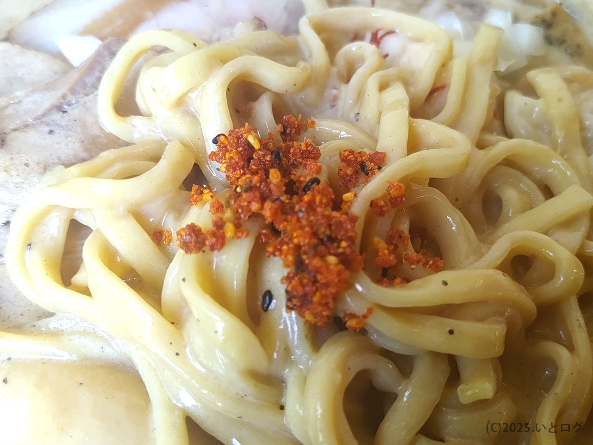 もちもち平打ち麺に自家製辛味スパイスをオン。麺肌にソースが絡むアップ。