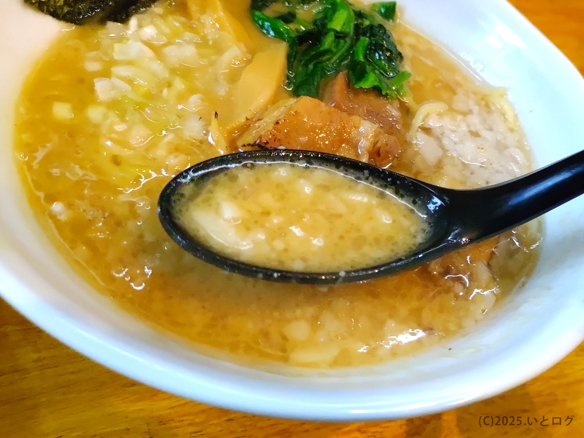 背脂と刻み玉ねぎが浮かぶ豚骨醤油スープをレンゲですくい上げたところ