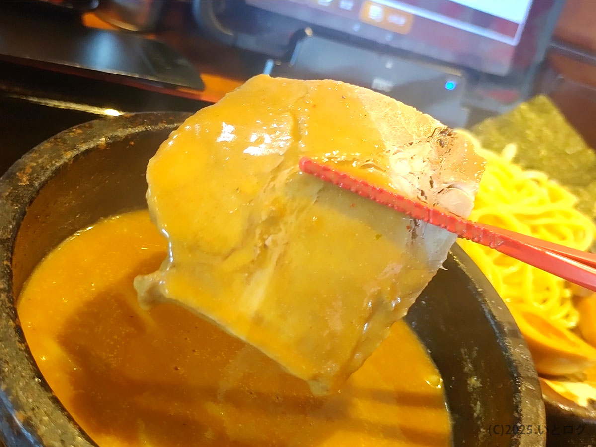 厚切りチャーシューを石鍋つけ汁に浸して味わう、竹本商店 つけ麺の一場面