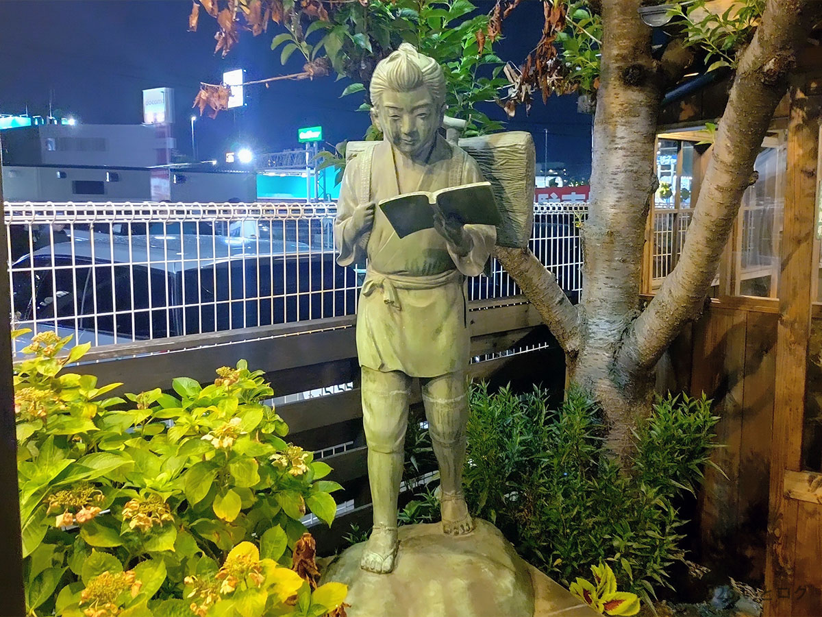 久留米とんこつラーメン松山分校の店先に立つ読書姿の像。松山で久留米ラーメンを味わえる一軒