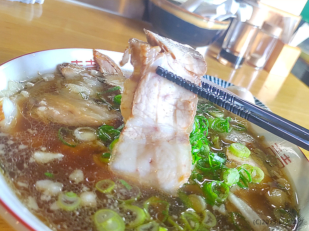 麺 㐂色のラーメン。箸で持ち上げたチャーシューは肉厚で、レビューでも人気のおすすめトッピング。