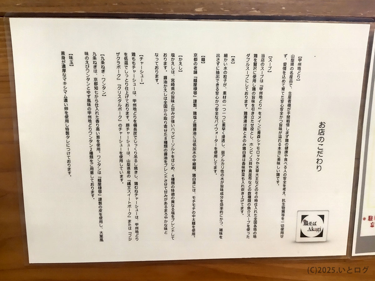 鶏そばAkari（甲府）の店内に掲示された、スープや地鶏など素材のこだわりを説明した案内ボード。鶏白湯スープに使用している食材や調理方針が詳細に記載されている。