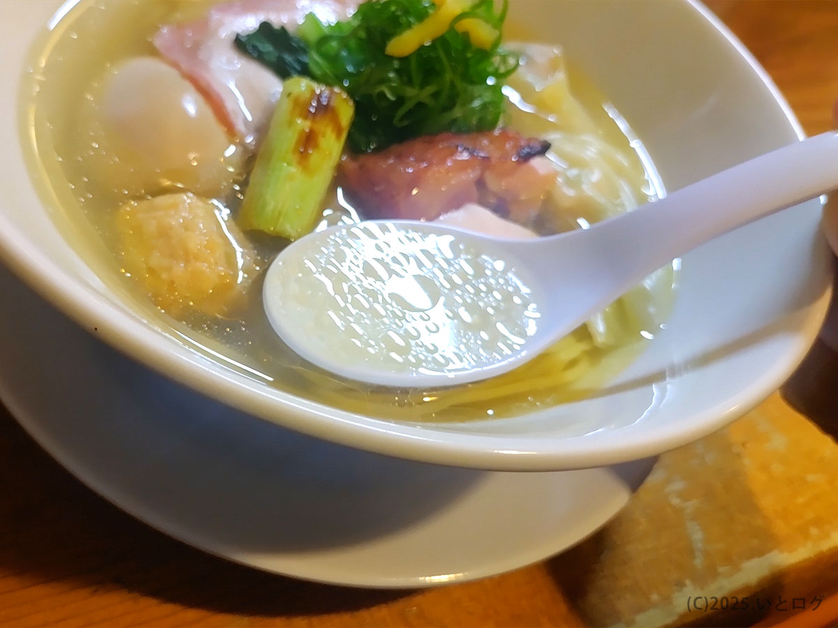 鶏そばAkari（甲府）の鶏白湯スープをレンゲで掬い上げた様子。黄金色のスープ表面に油膜が浮き、鶏出汁の香りが想像できる写真。山梨で人気の鶏系ラーメンを探す人に向けた一枚。