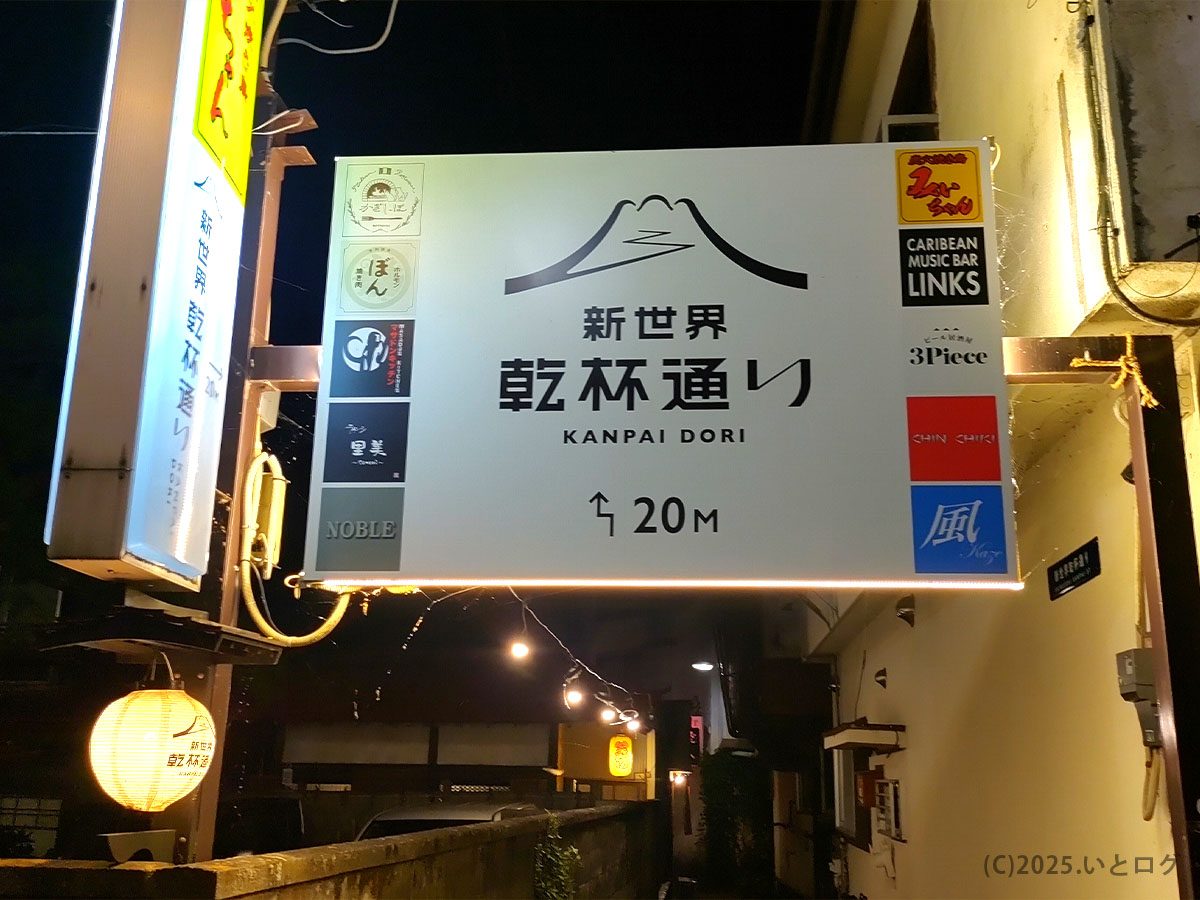 「富士吉田市の新世界乾杯通りの入口。明かりに照らされた看板に『KANPAI DORI』の文字。夜の富士急ハイランド近く、中華蕎麦よるのふじがあるエリア。」