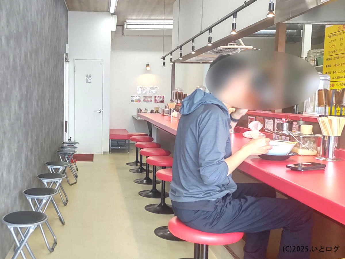 赤いカウンターが伸びる近江道家 彦根店の店内。待機スツールも整い、客がゆったりラーメンをすする落ち着いた空間。