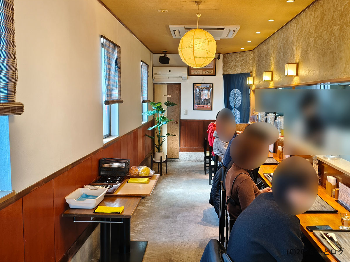 入鹿TOKYO本店の店内カウンター席の様子。落ち着いた和モダンな空間でラーメンを待つ客の姿。