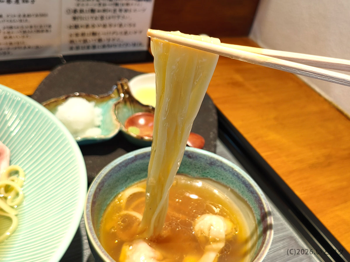 入鹿TOKYOの昆布水つけ麺をつけ汁にくぐらせて持ち上げた様子。自家製麺の質感が分かる。