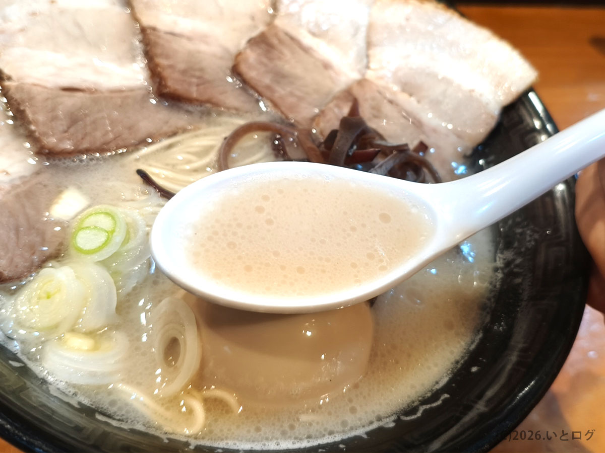 万力屋 ラーメンの豚骨スープをれんげですくった様子。山梨ラーメンらしい濃厚な白濁スープ