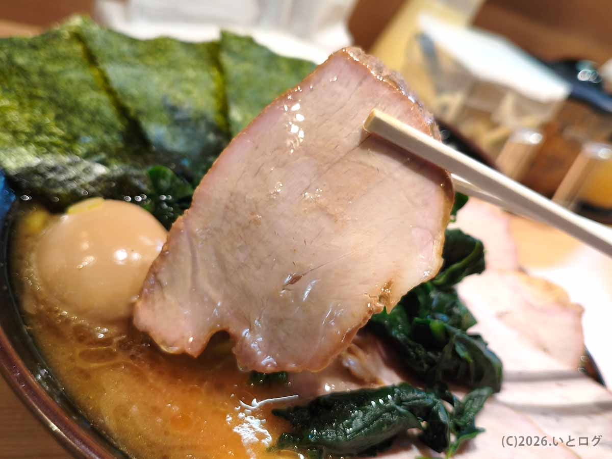 池袋の家系ラーメン店「皇綱家」のラーメンにのったチャーシューを箸で持ち上げた写真。しっとりした肉質と濃厚スープの組み合わせが見える。