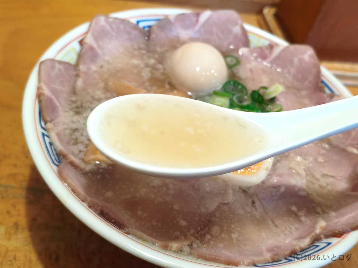 はまんどラーメンのスープをレンゲですくった様子。背脂の浮いた淡い色のスープと、丼いっぱいに並ぶチャーシューが見える。