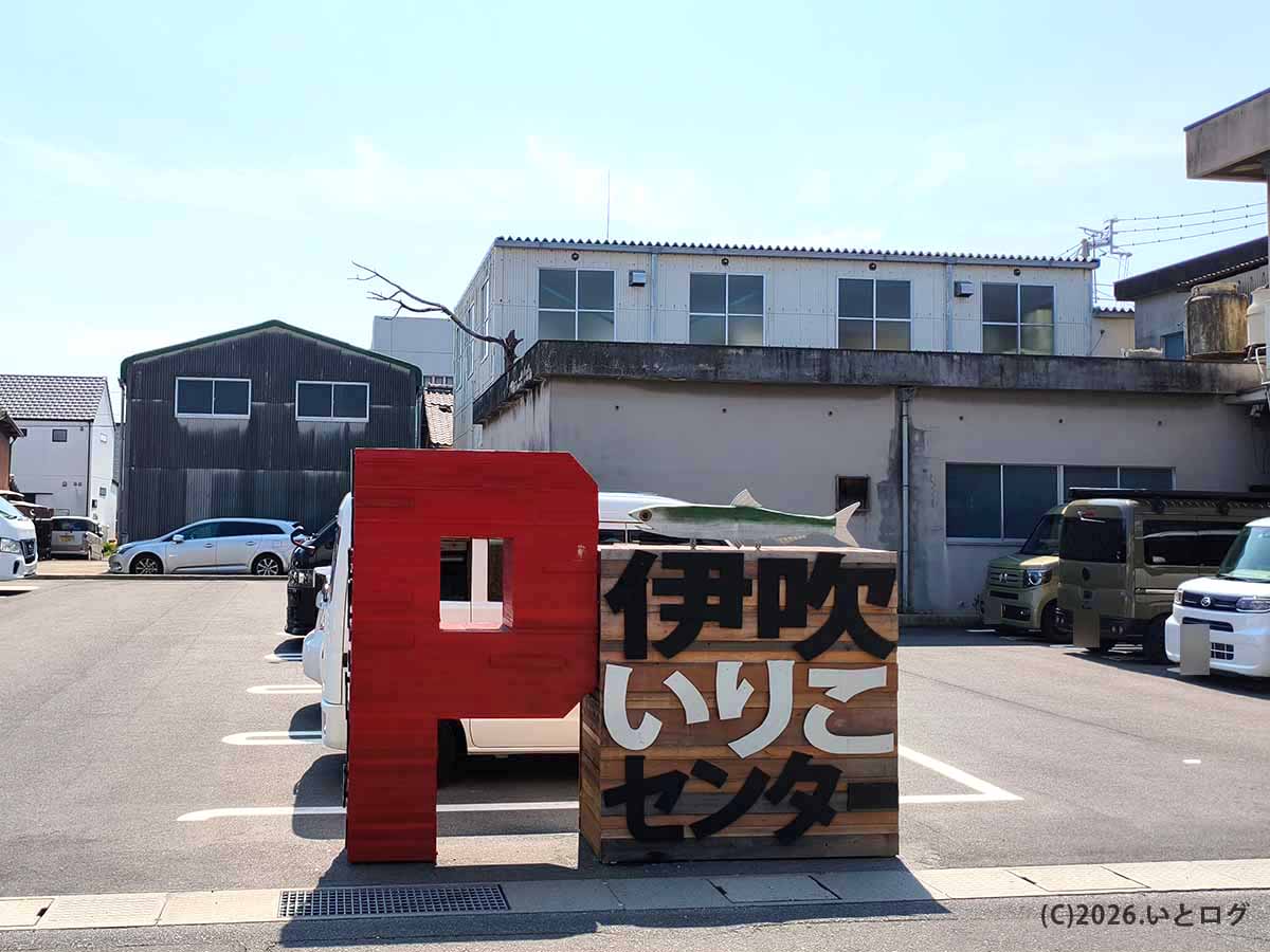 香川県観音寺市にある讃岐らぁ麺 伊吹いりこセンターの駐車場前に立つ木製看板と赤いオブジェ