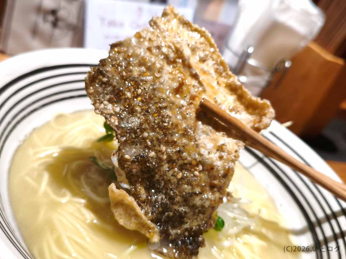 箸で持ち上げた、パリッと焼かれてゴマと香辛料が振られた堂の浦の鯛塩ラーメンの鯛皮