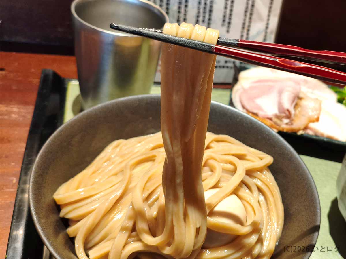 箸で持ち上げた、艶やかで幅のあるつけ麺 繁田の自家製極太麺
