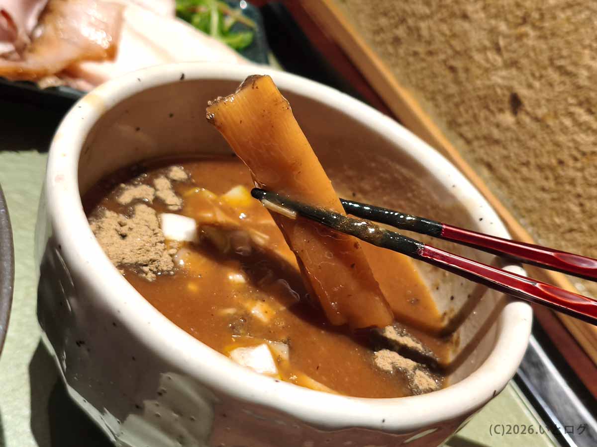 濃厚なつけ汁から箸で持ち上げた、つけ麺 繁田の厚みがある極太メンマ