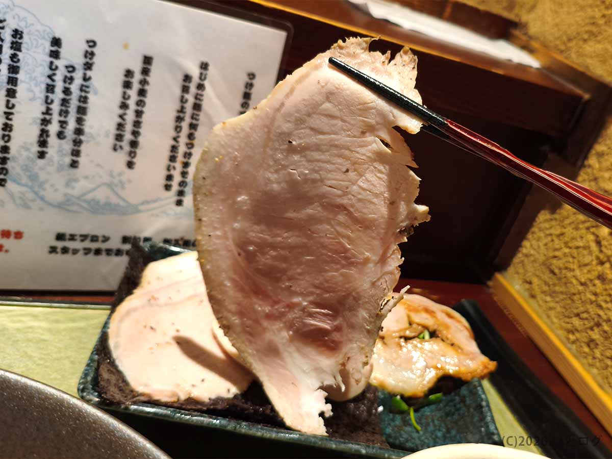 箸で持ち上げた、淡いピンク色で大判に仕上げられたつけ麺 繁田の低温調理チャーシュー