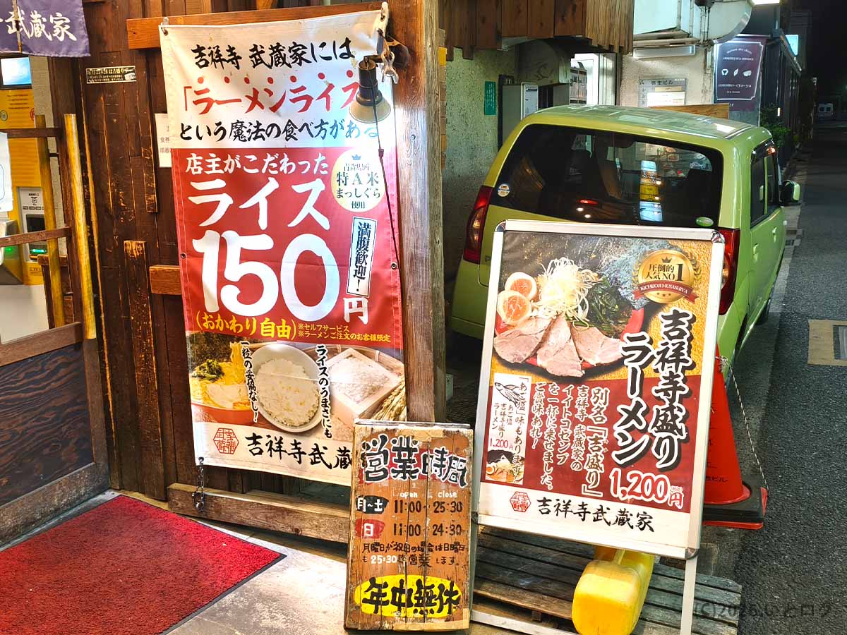 東京都武蔵野市吉祥寺にある家系ラーメン店「吉祥寺武蔵家 本店」の外観。吉祥寺盛りラーメンやライス150円、営業時間を案内する看板が並ぶ