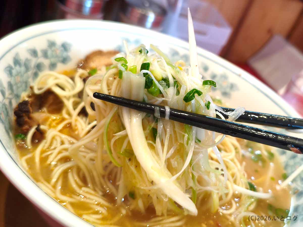 宮崎・都城のラーメンいってつで、たっぷりの白髪ねぎと細麺を一緒に箸で持ち上げて食べる様子