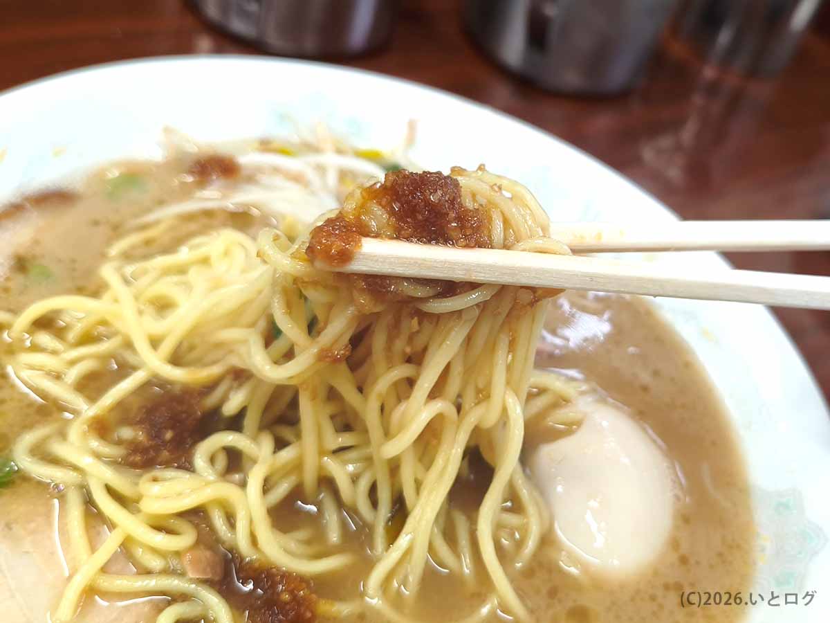ラーメン洋の中細麺に卓上調味料を合わせて箸で持ち上げた様子。豚骨ラーメンを味変して楽しめる