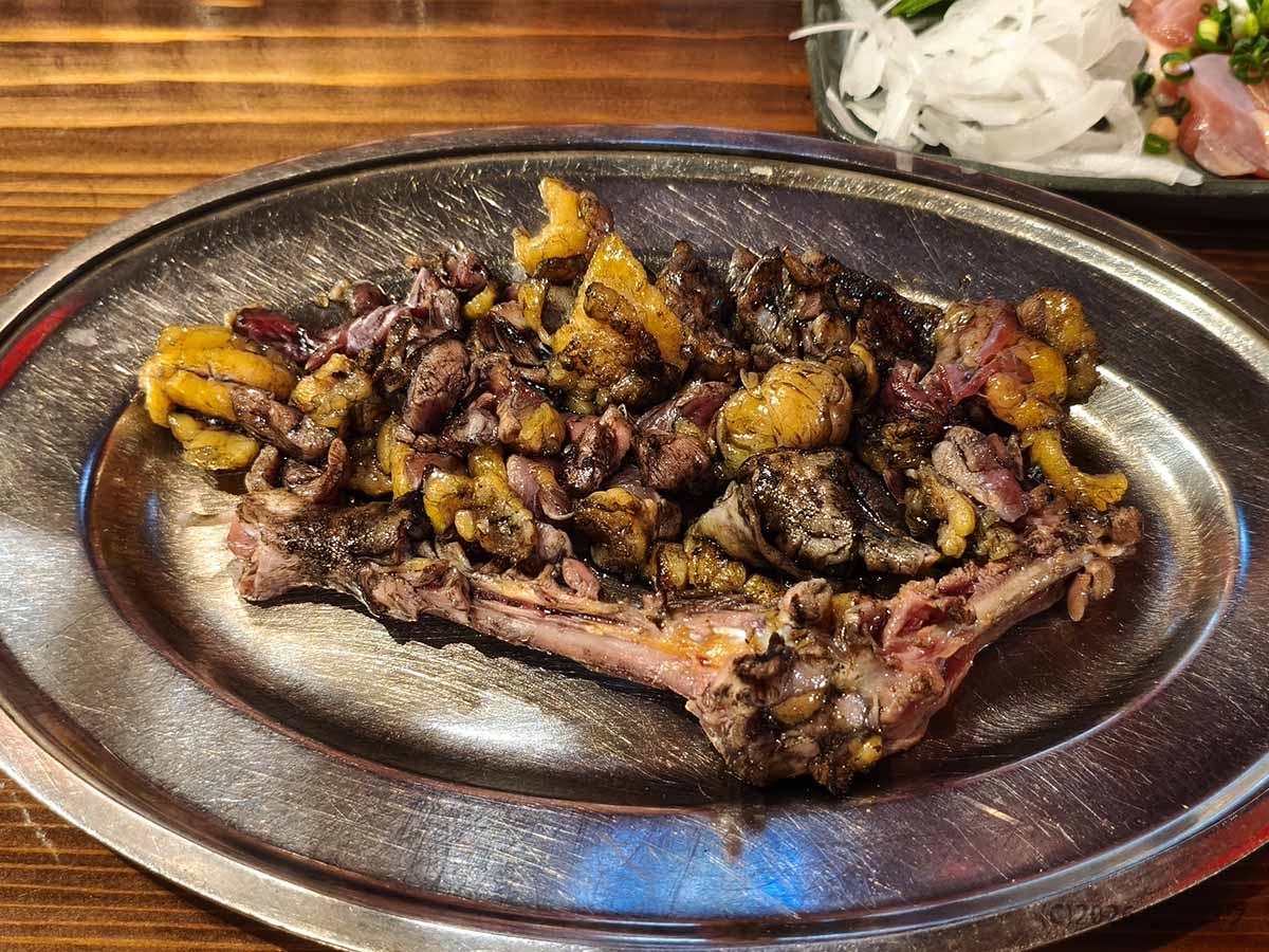 丸万焼鳥 支店の名物もも焼き。炭火で黒く香ばしく焼かれた鶏肉が骨付きのまま盛られている