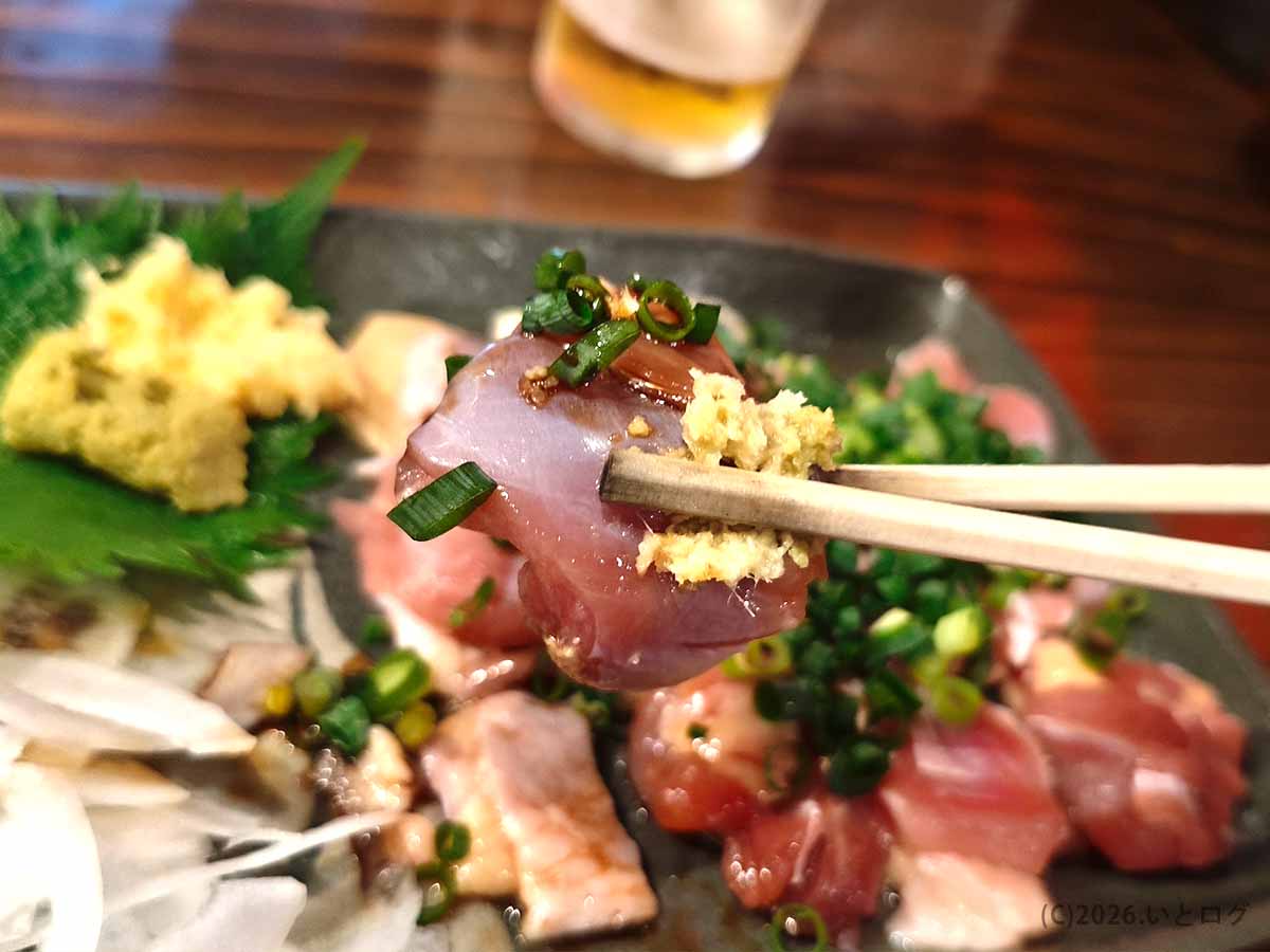 丸万焼鳥 支店の鳥刺しを箸で持ち上げた様子。新鮮な鶏肉に生姜やねぎなどの薬味を添えている