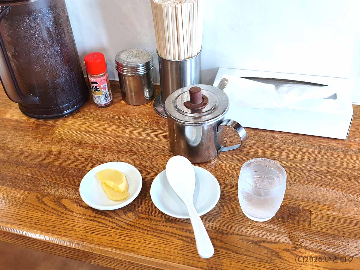 らーめん本舗 さといも 本店の卓上セット。調味料や箸、水とともにたくあんが用意されている