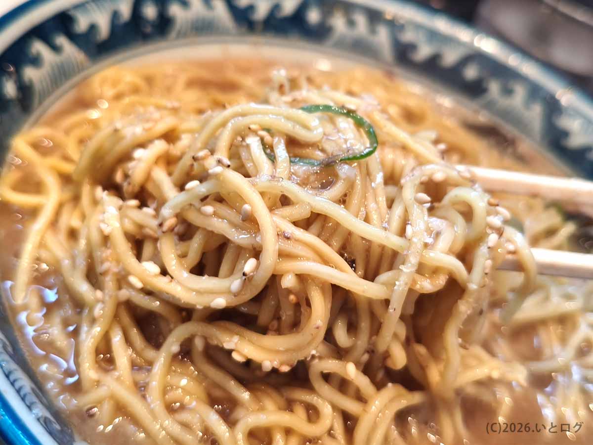 風来軒 加納本店のとんこつラーメンに卓上のゴマを加え、濃厚な豚骨スープと麺を絡めていただく様子