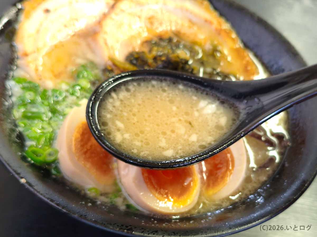 れんげで黒いスープをすくい上げる様子。背脂が適度に浮いた、コクの深そうな月乃家の特製ラーメンスープ。