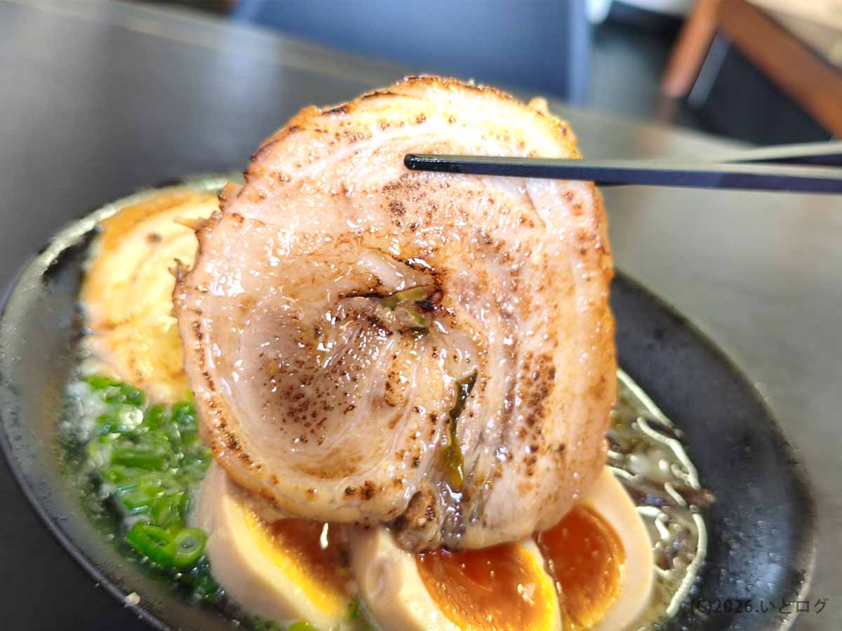 箸で持ち上げられた、大ぶりで香ばしく炙られた月乃家の絶品巻きチャーシュー。山梨ラーメン巡りでもおすすめのトッピング。