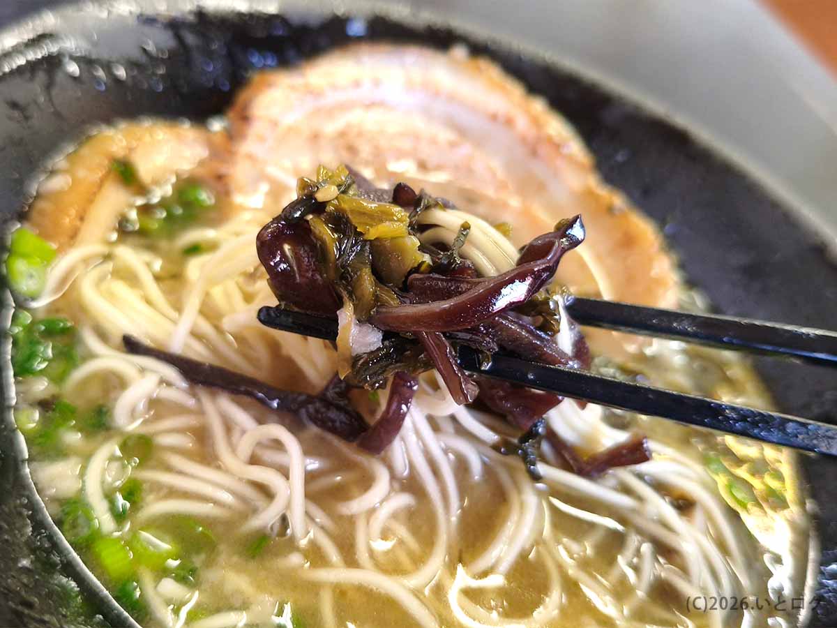 箸で持ち上げられたラーメンのトッピング。豚骨スープの美味しさを引き立てるコリコリとしたキクラゲと高菜。